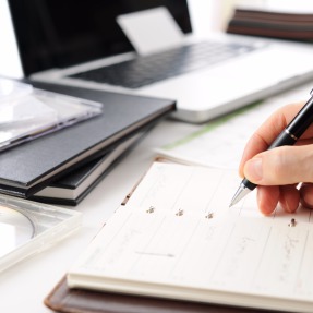 A hand on top of a planner with a laptop behind